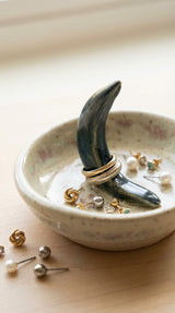 Handmade ceramic jewelry dish with crescent moon ring holder holding gold and silver rings on wooden surface